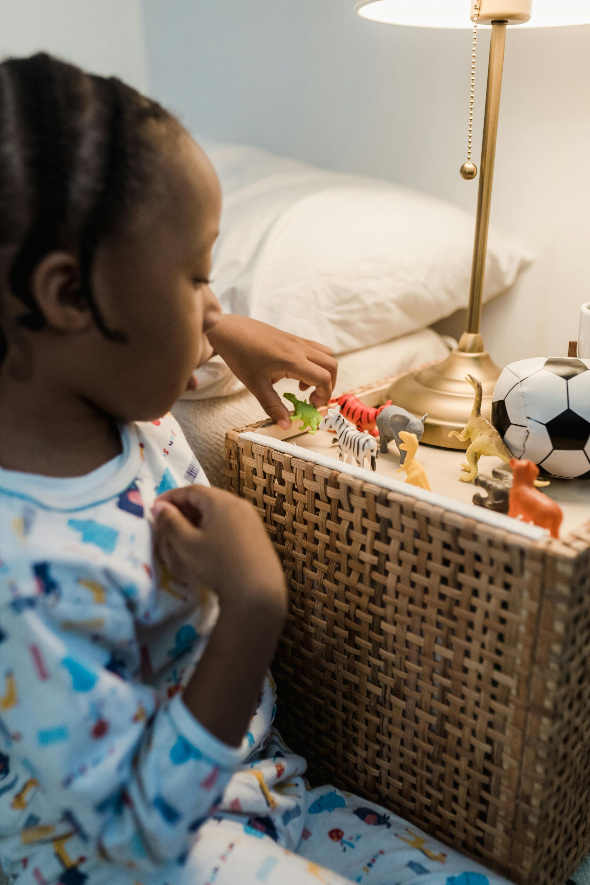A little girl is sitting on a nightstand playing with toys.