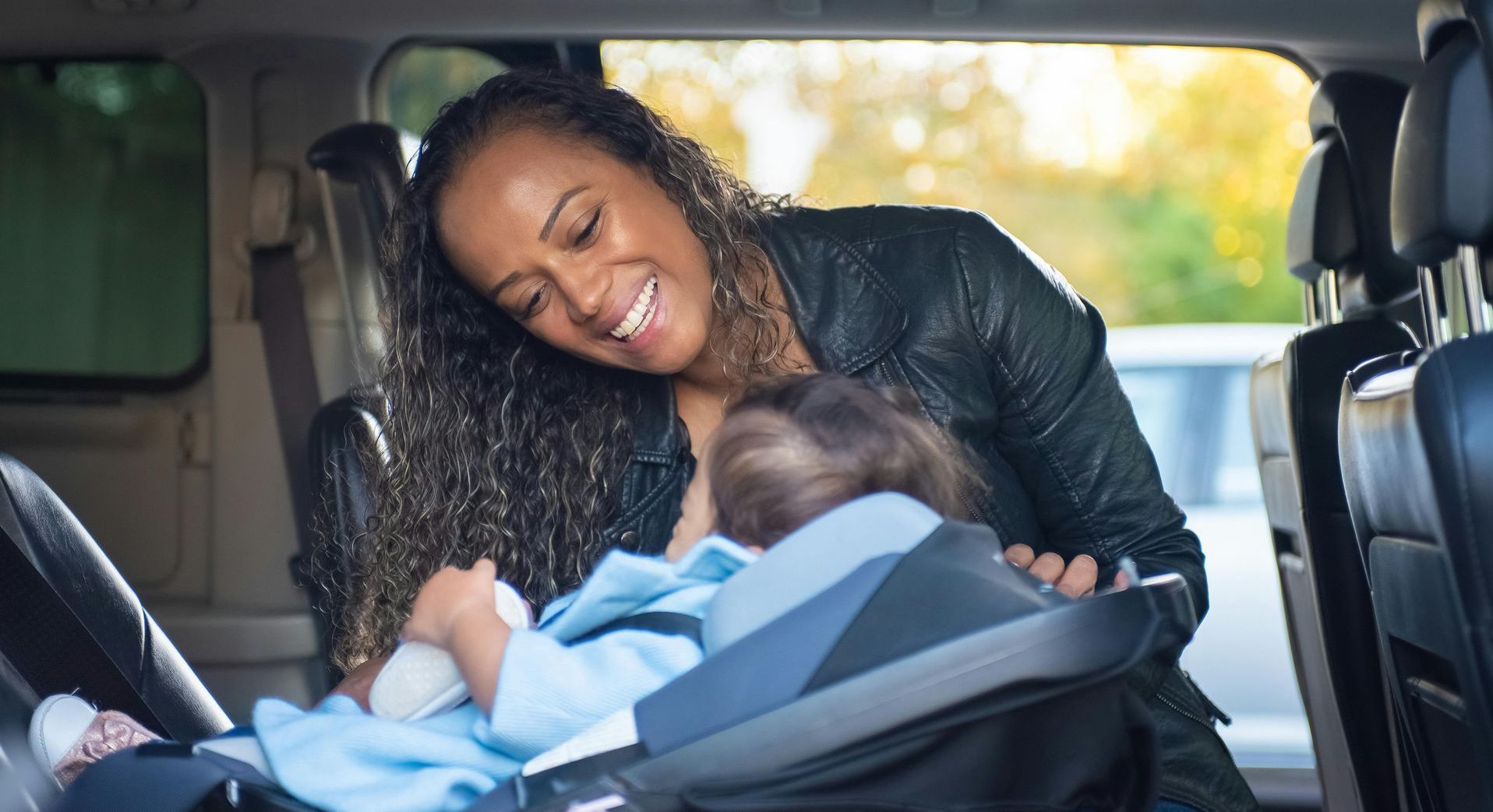 A woman is putting a baby in a car seat.