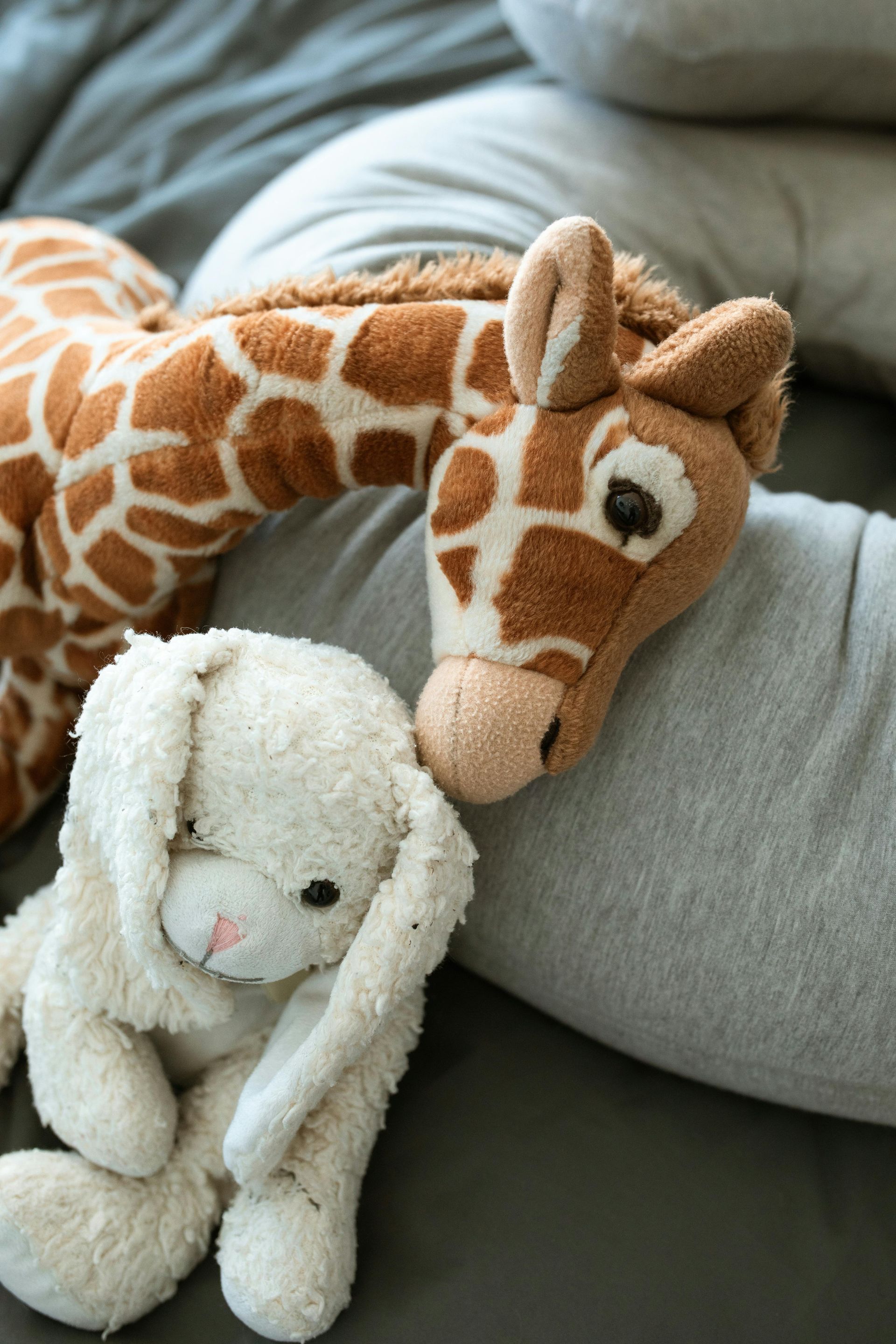 A stuffed giraffe and a stuffed rabbit are laying on a pillow.