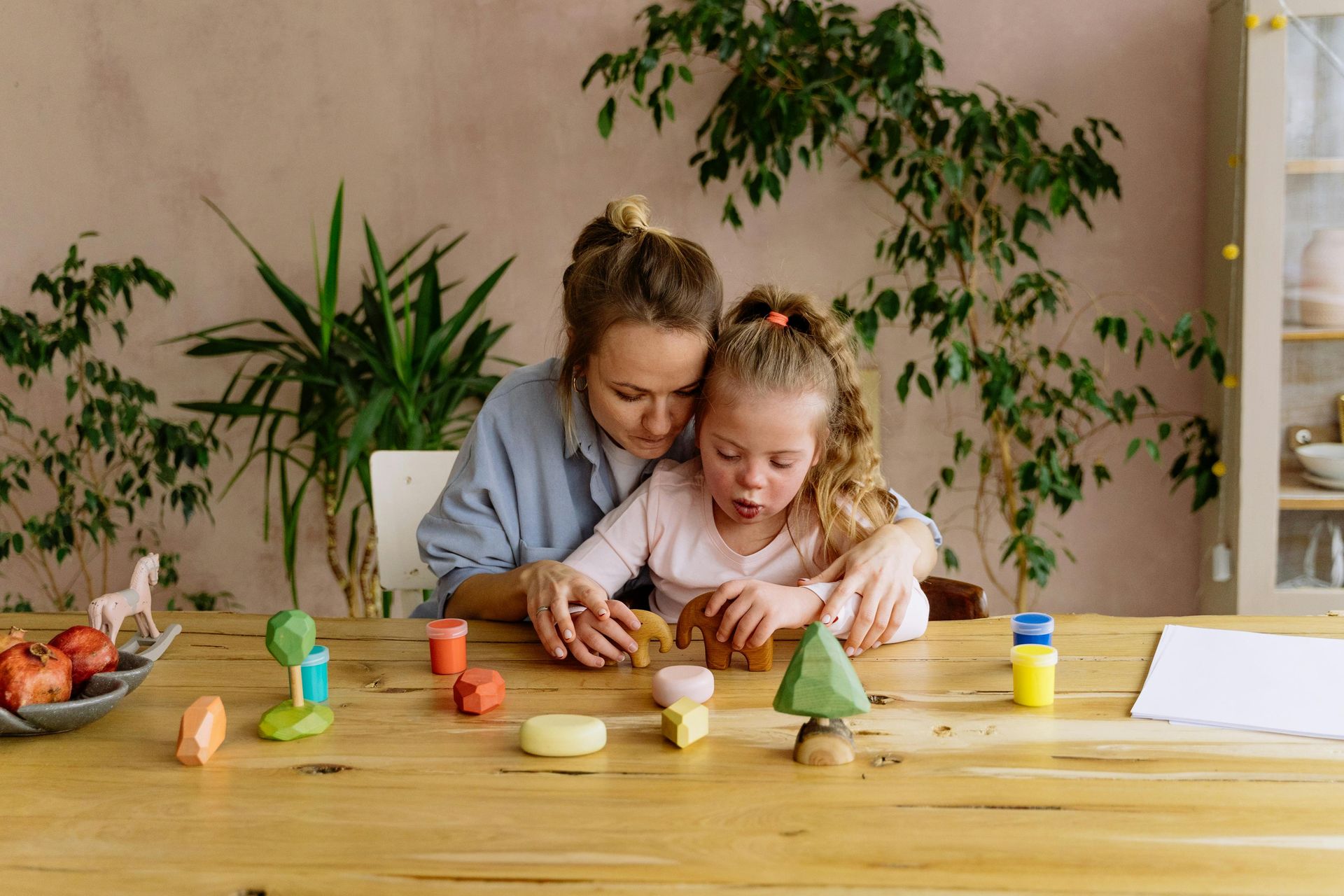 A woman and a little girl are sitting at a table playing with toys.