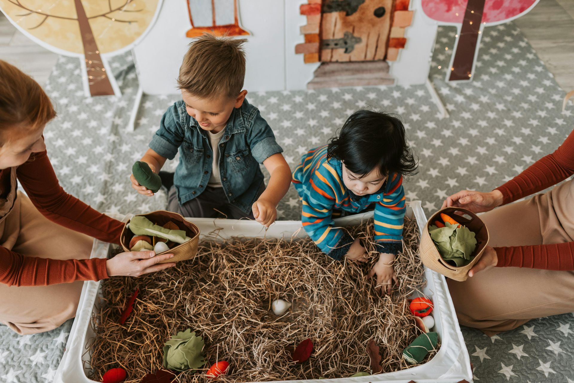 A group of children are playing in a sensory bin filled with hay and vegetables.