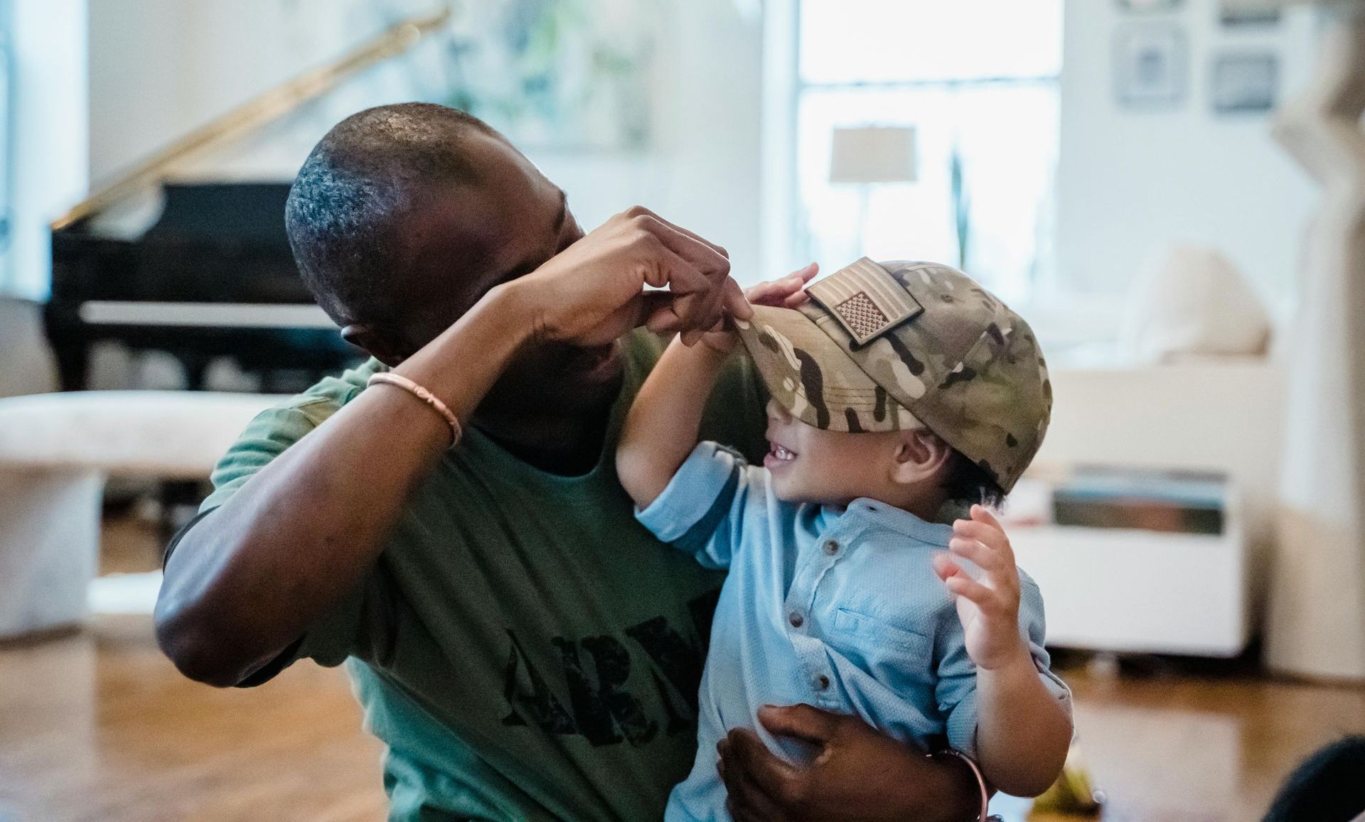 A man is putting a hat on a little boy in a living room.