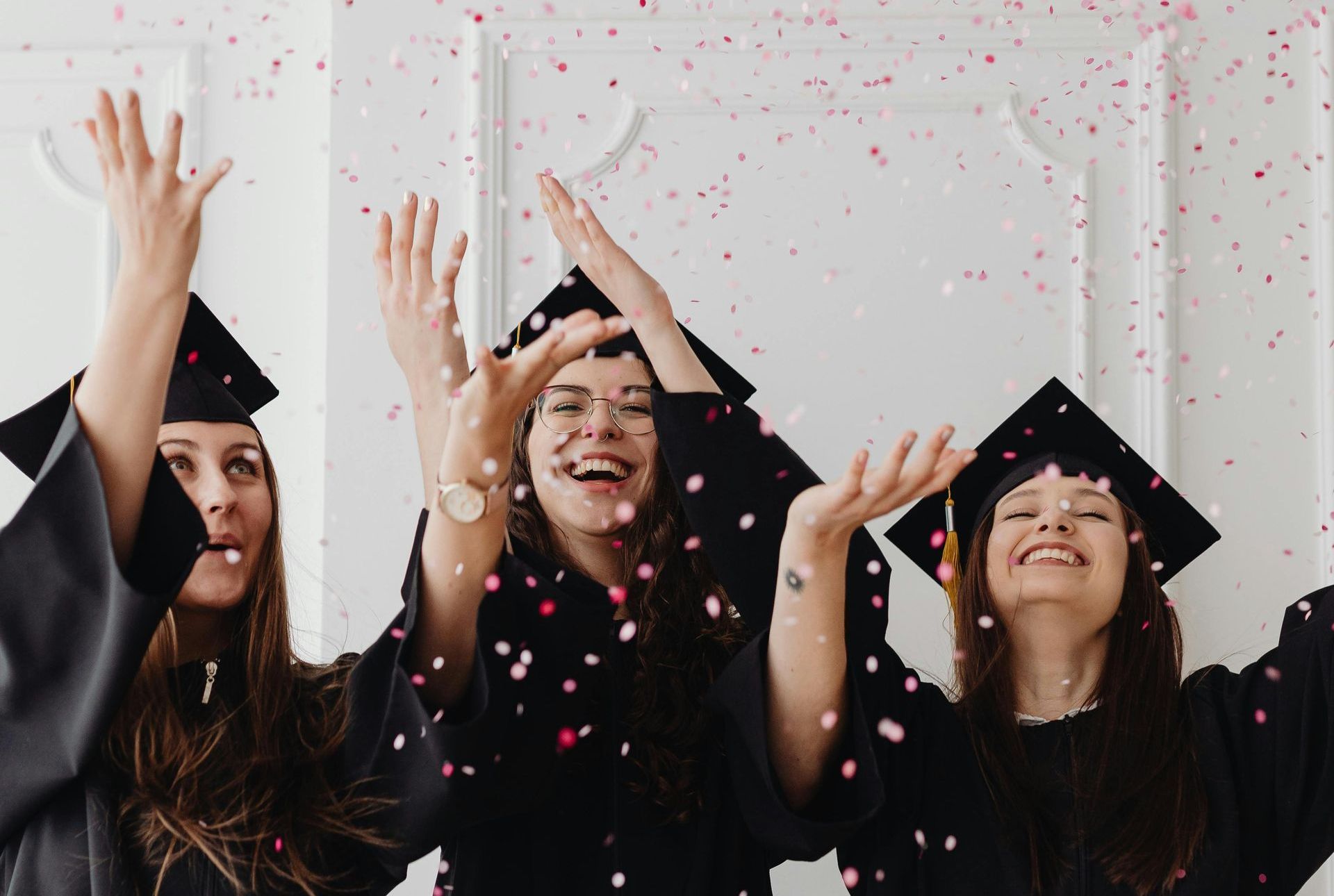 Three female graduates are throwing confetti in the air.