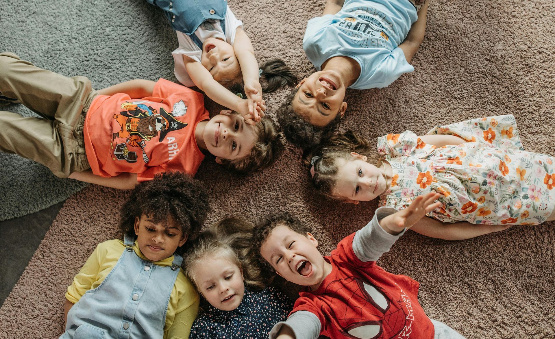 A group of children are laying in a circle on the floor.