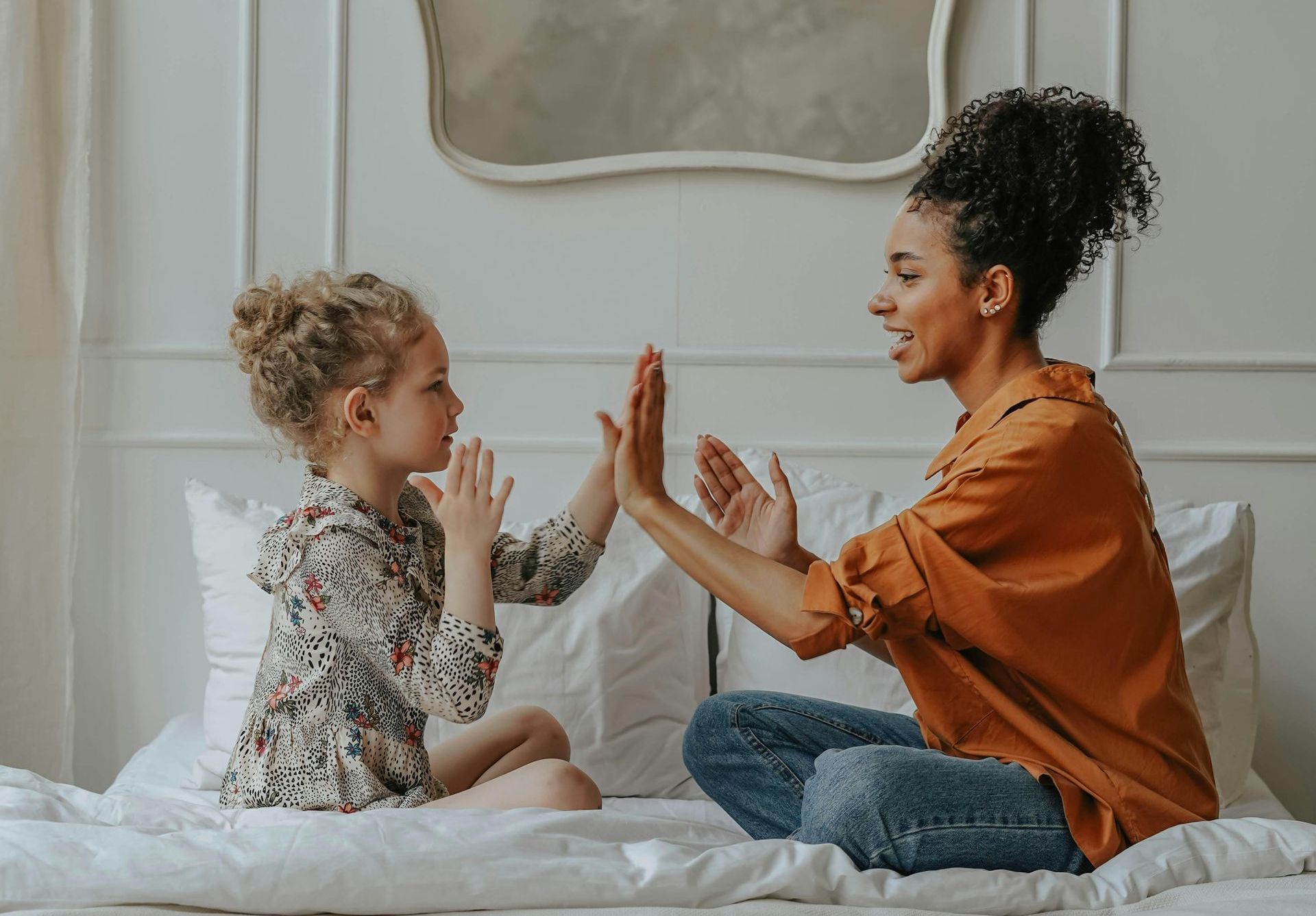 A woman and a little girl are sitting on a bed giving each other a high five.