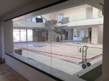 Large glass wall reveals an expansive interior under construction, with a spiral staircase and unfinished flooring.