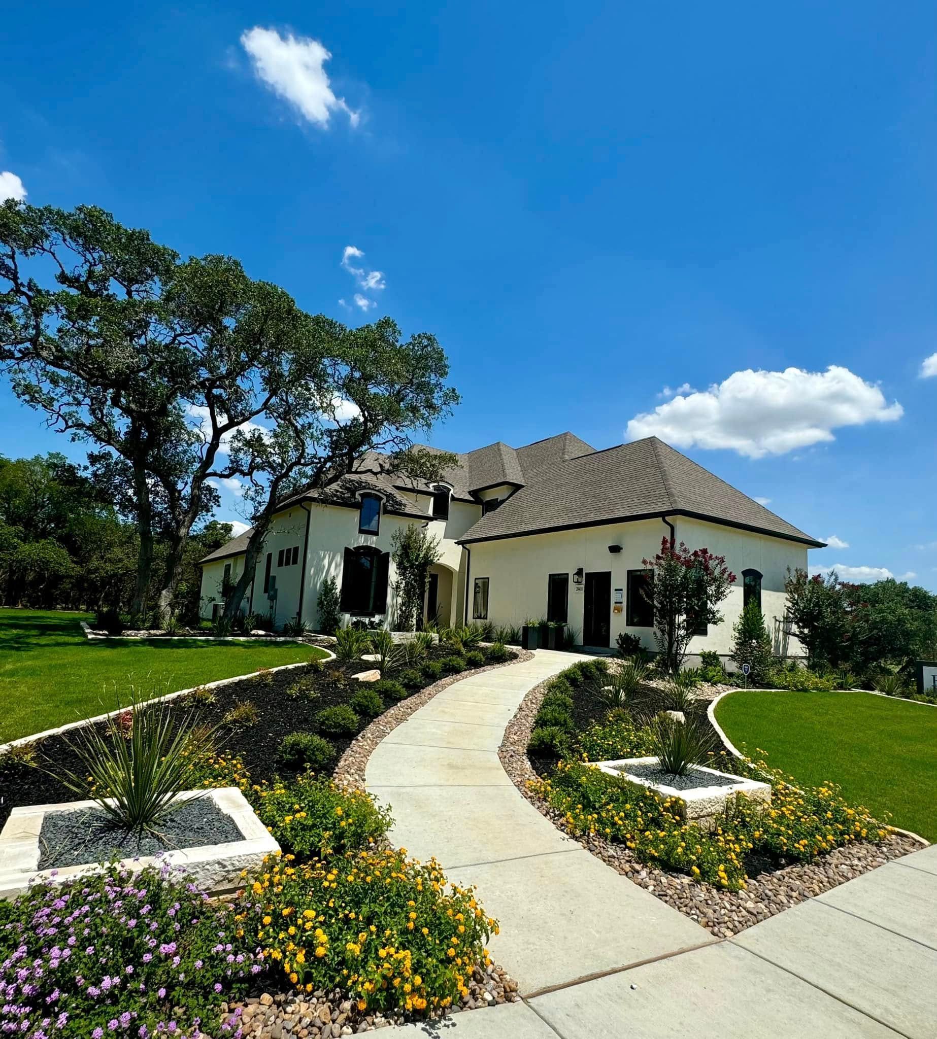Elegant white house with a winding walkway, lush landscaping, and a bright blue sky.
