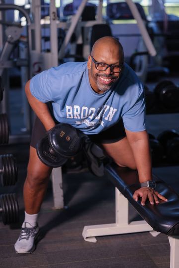 Johnny Lopez in a brooklyn shirt is lifting a dumbbell in a gym