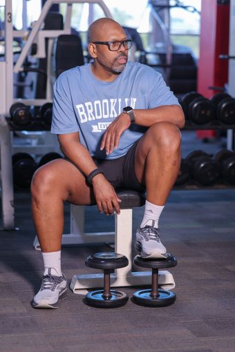 Johnny Lopez sitting on a bench in a gym next to dumbbells.