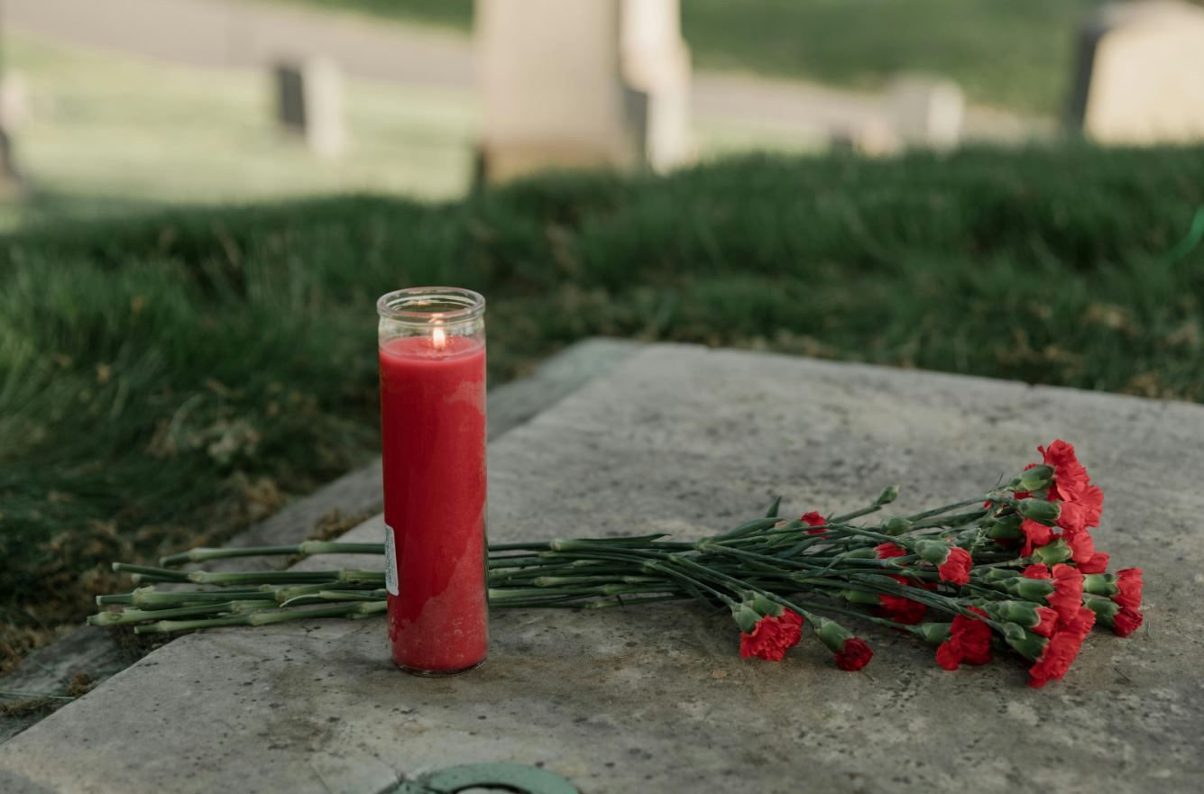 funeral remembrance scene with a prayer candle and red carnations laid at a cemetery grave in rio br