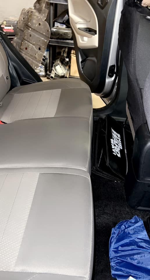 Car's open rear door reveals gray back seat. Black floor mat and door frame are visible.