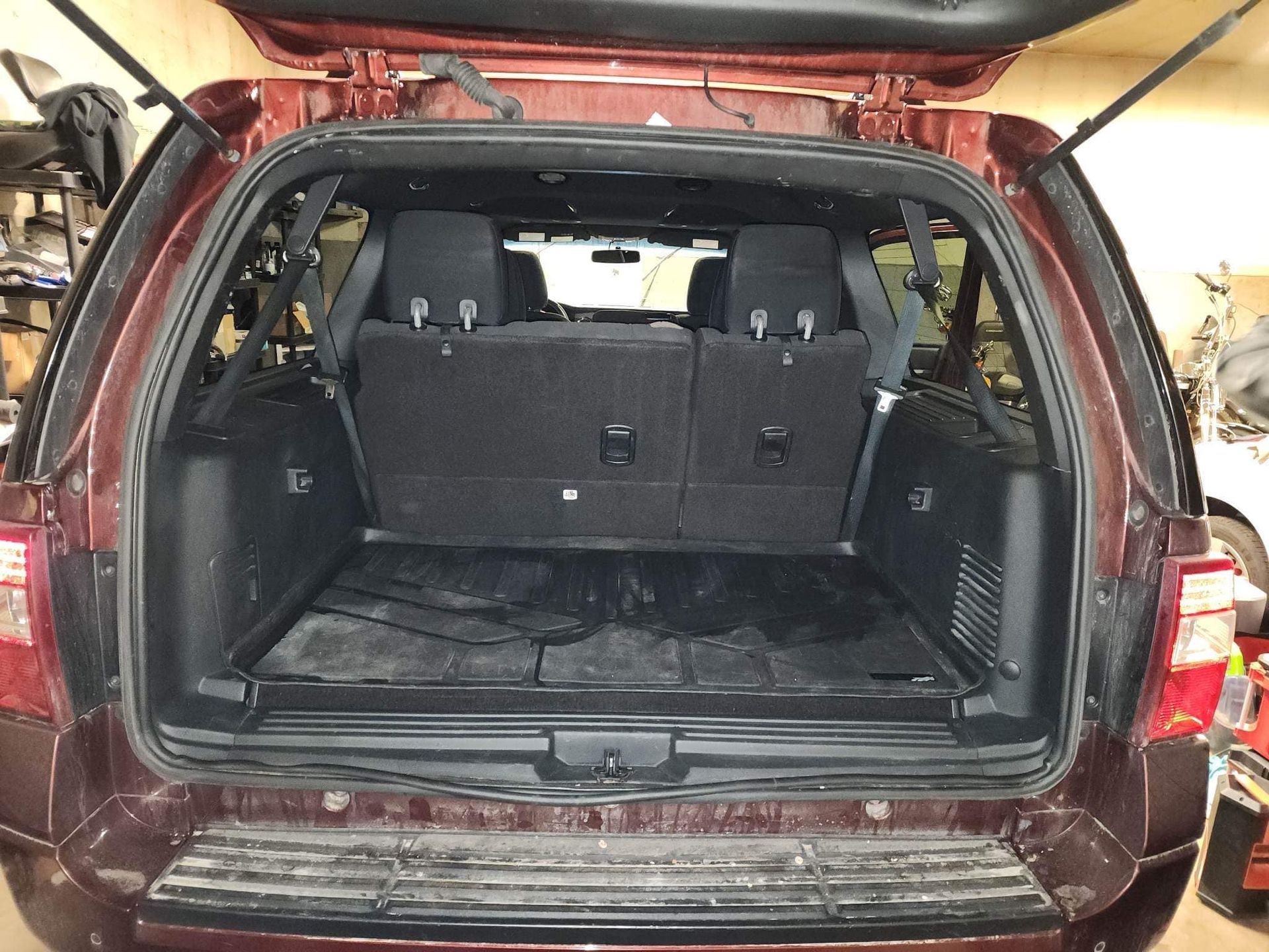 Open trunk of a red SUV with rear seats folded down, revealing cargo area with floor mats.