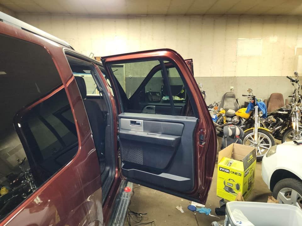 Red SUV with driver's side door open in a garage with tools and vehicles.