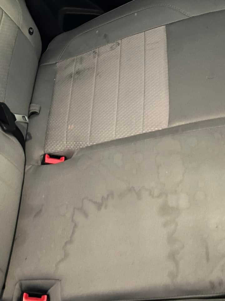 Gray car back seat with stains, including circular marks and dark spots.