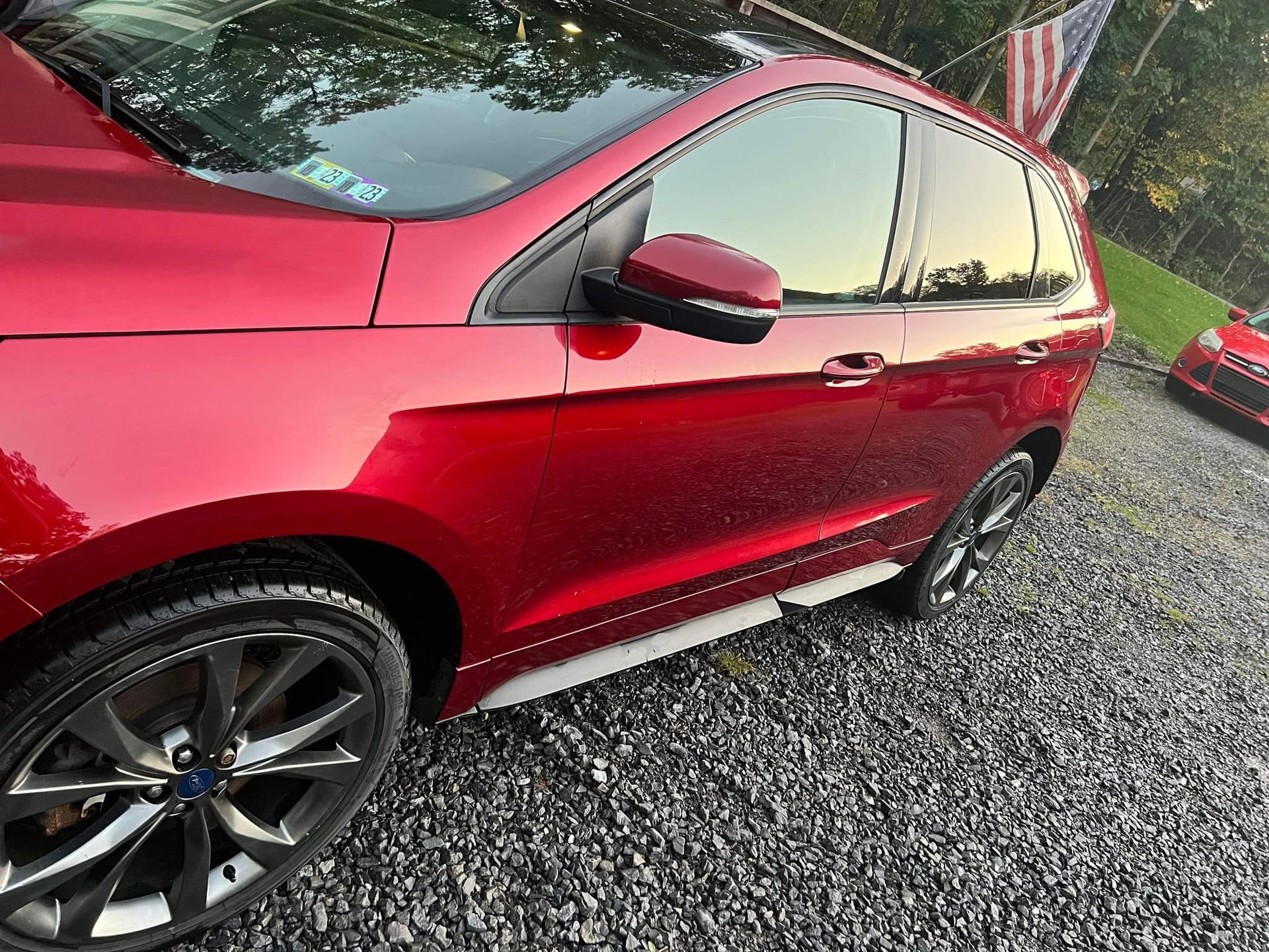 Red Ford Edge SUV parked on gravel, shiny exterior, black wheels.