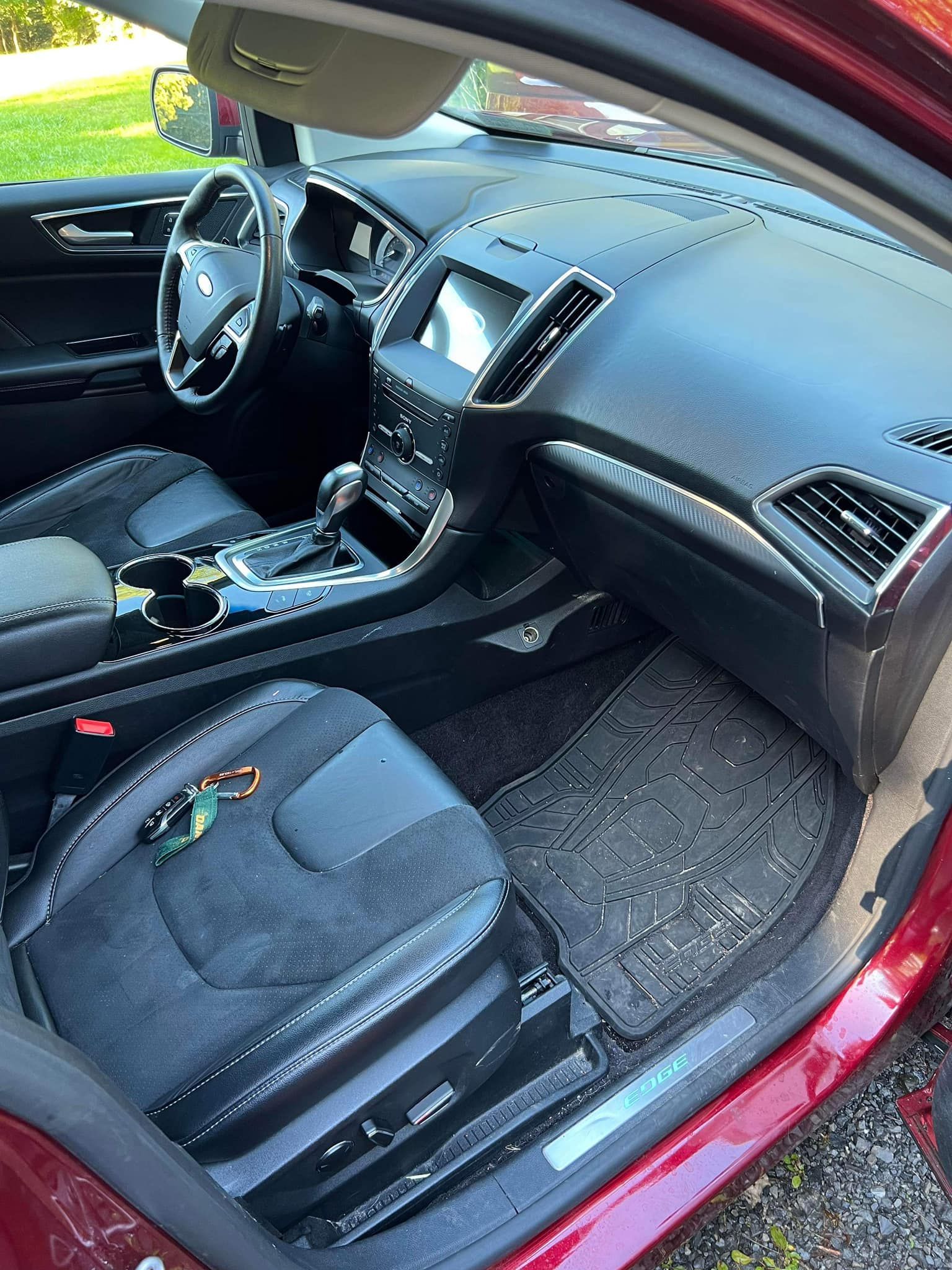 Interior of a red Ford Edge. Black dashboard, steering wheel, seats, and rubber floor mats.