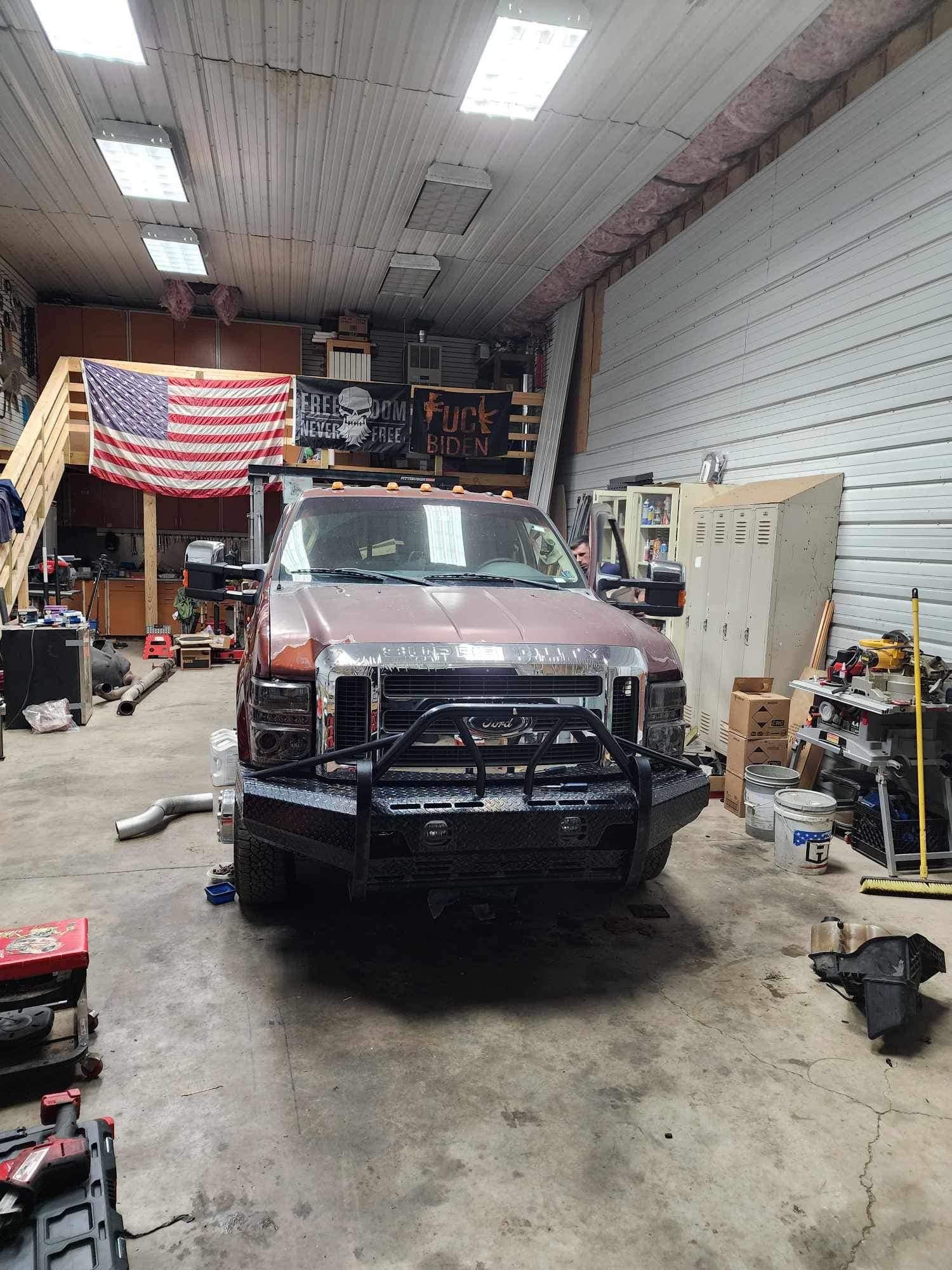 A brown Ford truck with a black bumper in a garage with an American flag.