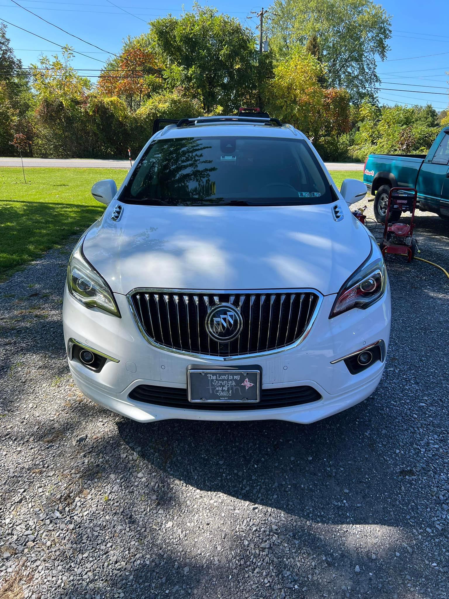 White Buick SUV parked on gravel driveway, under a sunny sky.