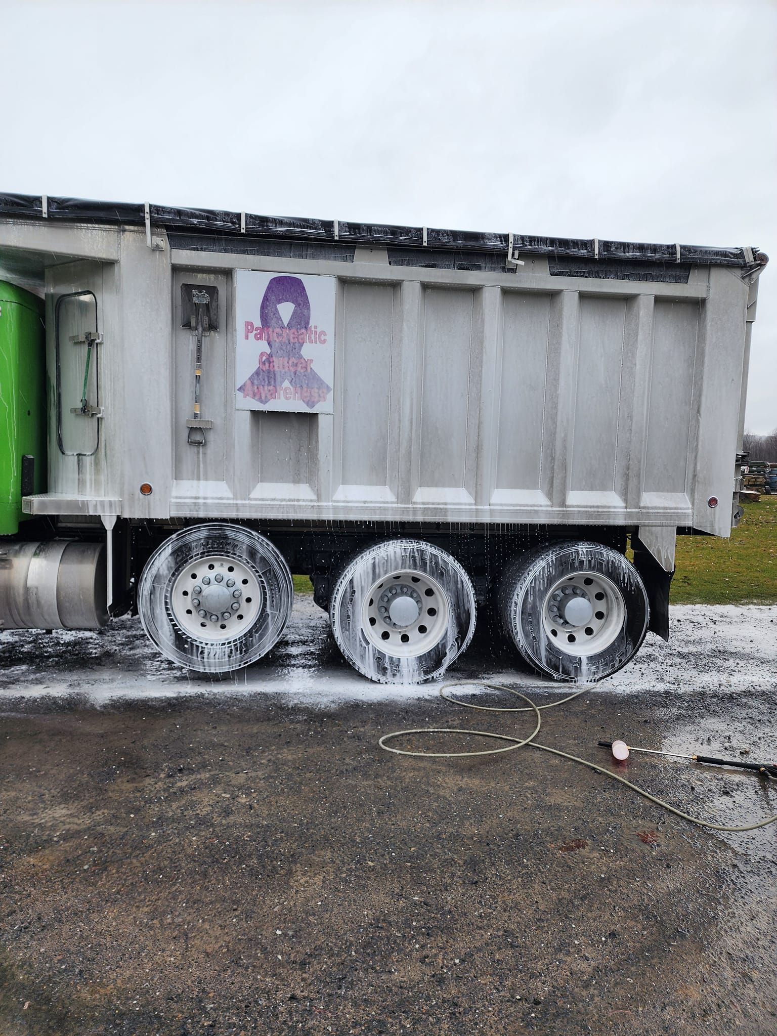 A large dump truck being washed with foamy soap. The wheels are covered in suds.