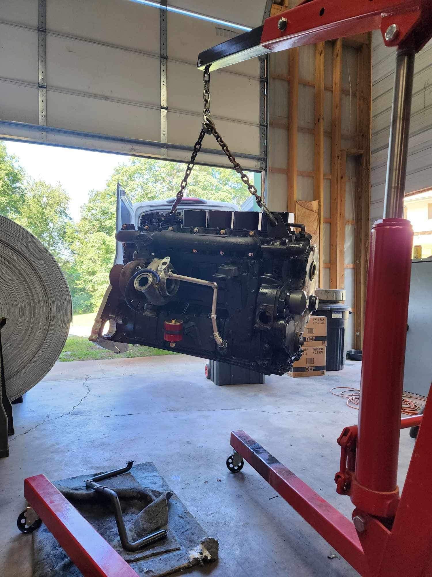 A large black engine suspended in a garage by a red hoist; preparing for removal.