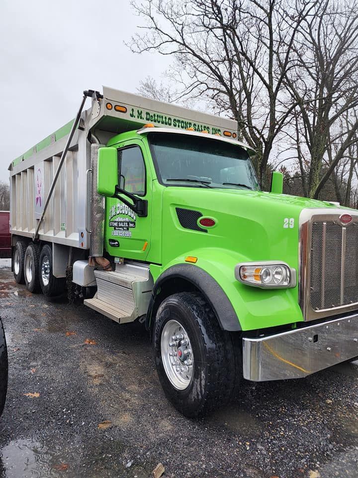 Bright green dump truck in a parking lot on a cloudy day.