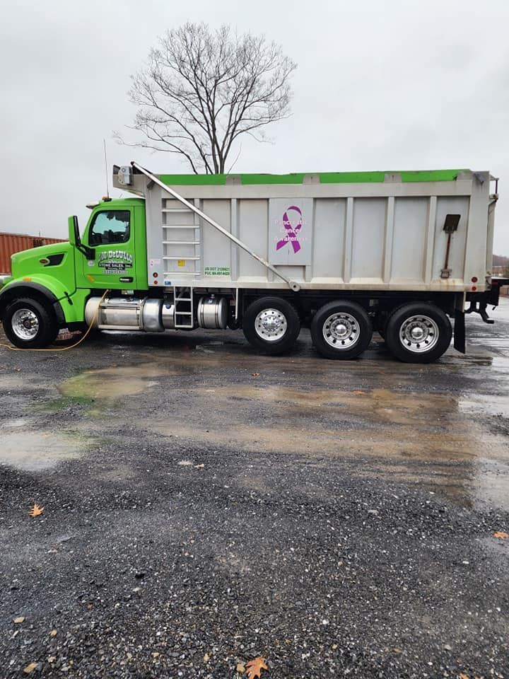 Green and silver dump truck parked on wet asphalt; a pink ribbon is on the side.