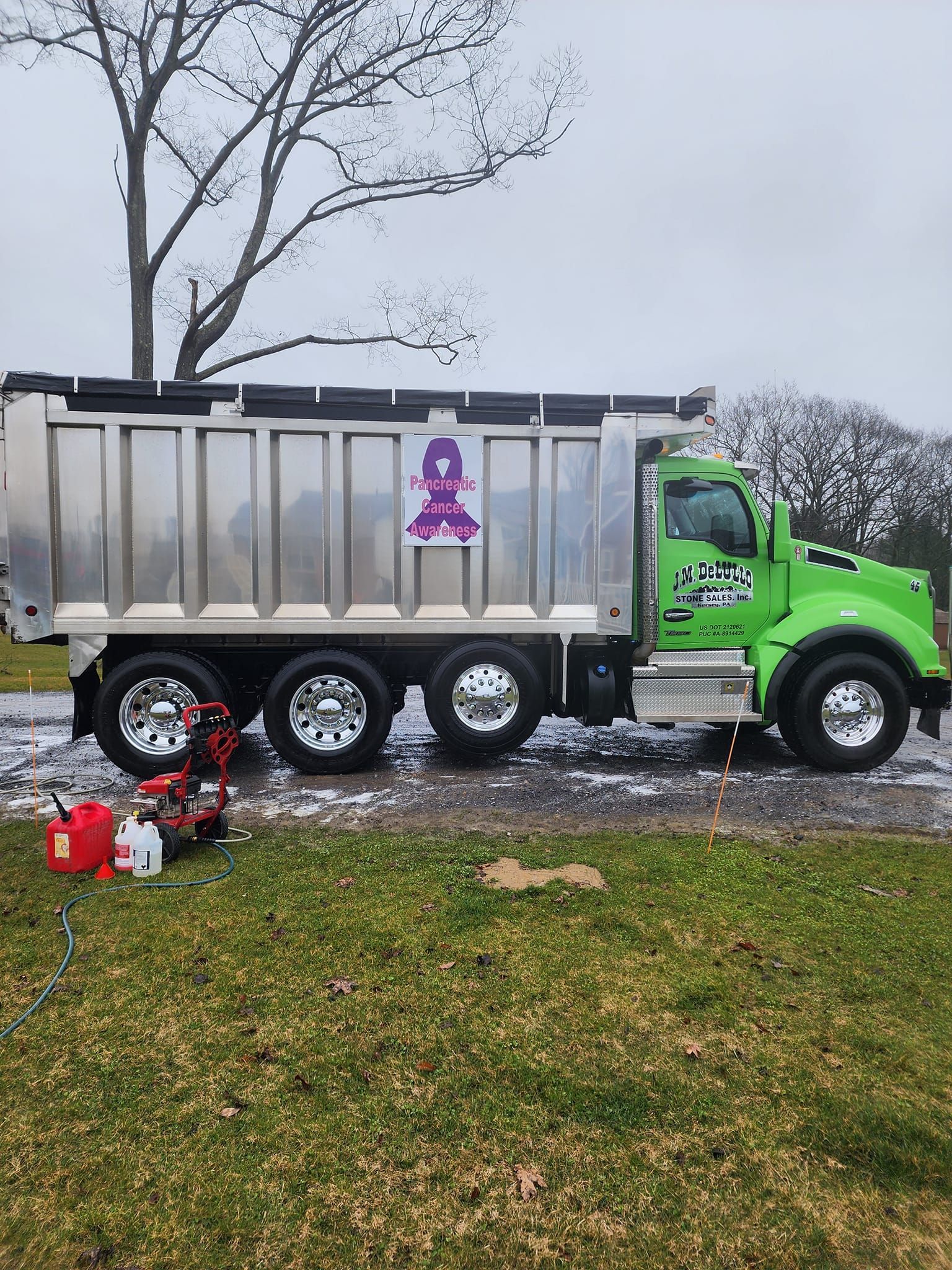 Green dump truck with a shiny silver bed parked on grass. A red and white power washer sits in front of the truck.