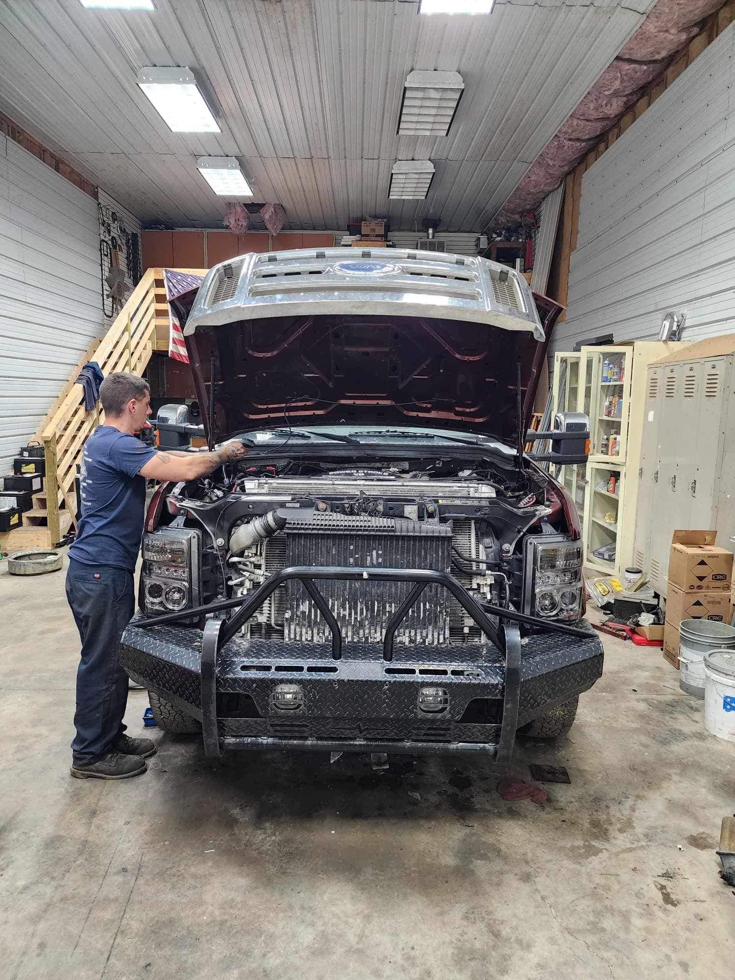 Mechanic working on a red pickup truck in a garage with the hood open.