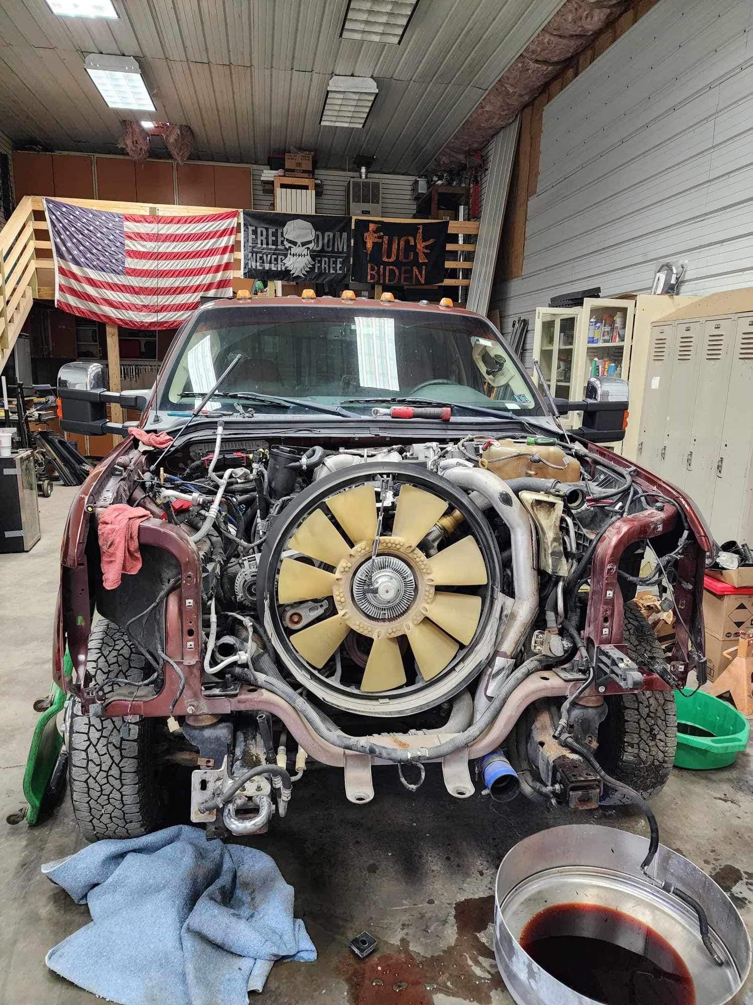 A red truck with its front end disassembled in a garage, with an American flag and tools visible.