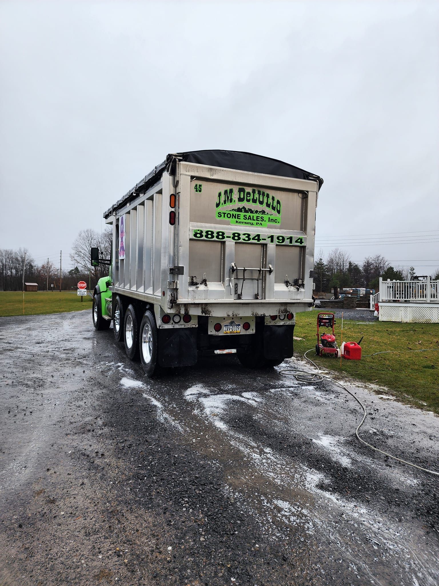 Green and silver dump truck parked on a gravel road, with the company name visible on the tailgate.