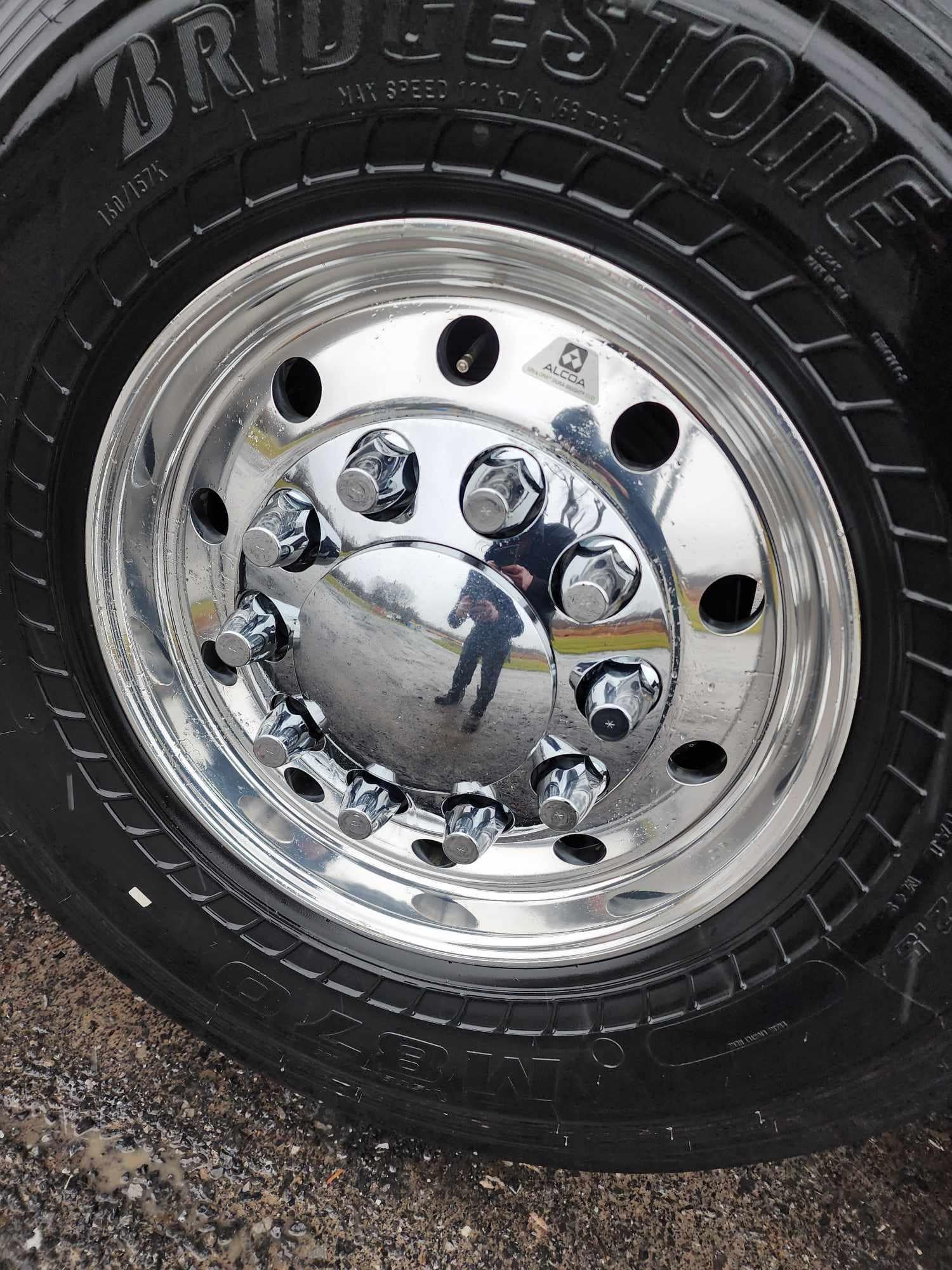 Shiny truck wheel with Bridgestone tire. Chrome hubcaps reflect person in the street.