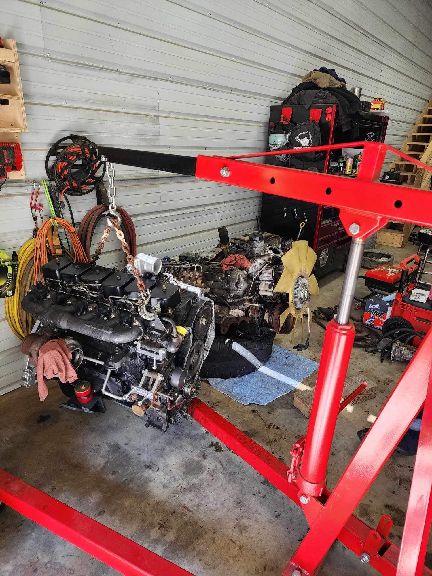 A red engine hoist lifting a black car engine in a garage setting.