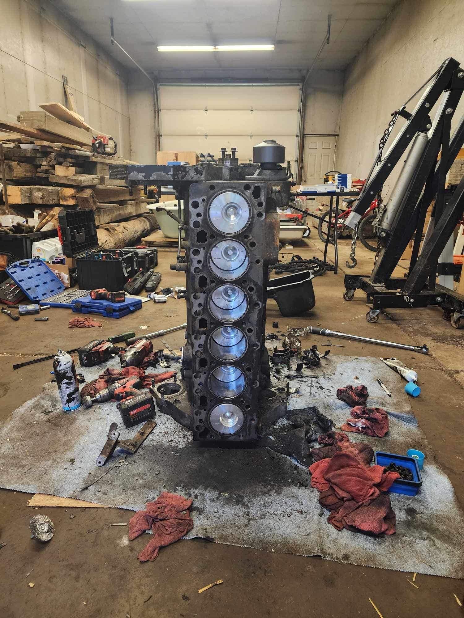 Engine block in a garage, surrounded by tools and parts, partially disassembled.