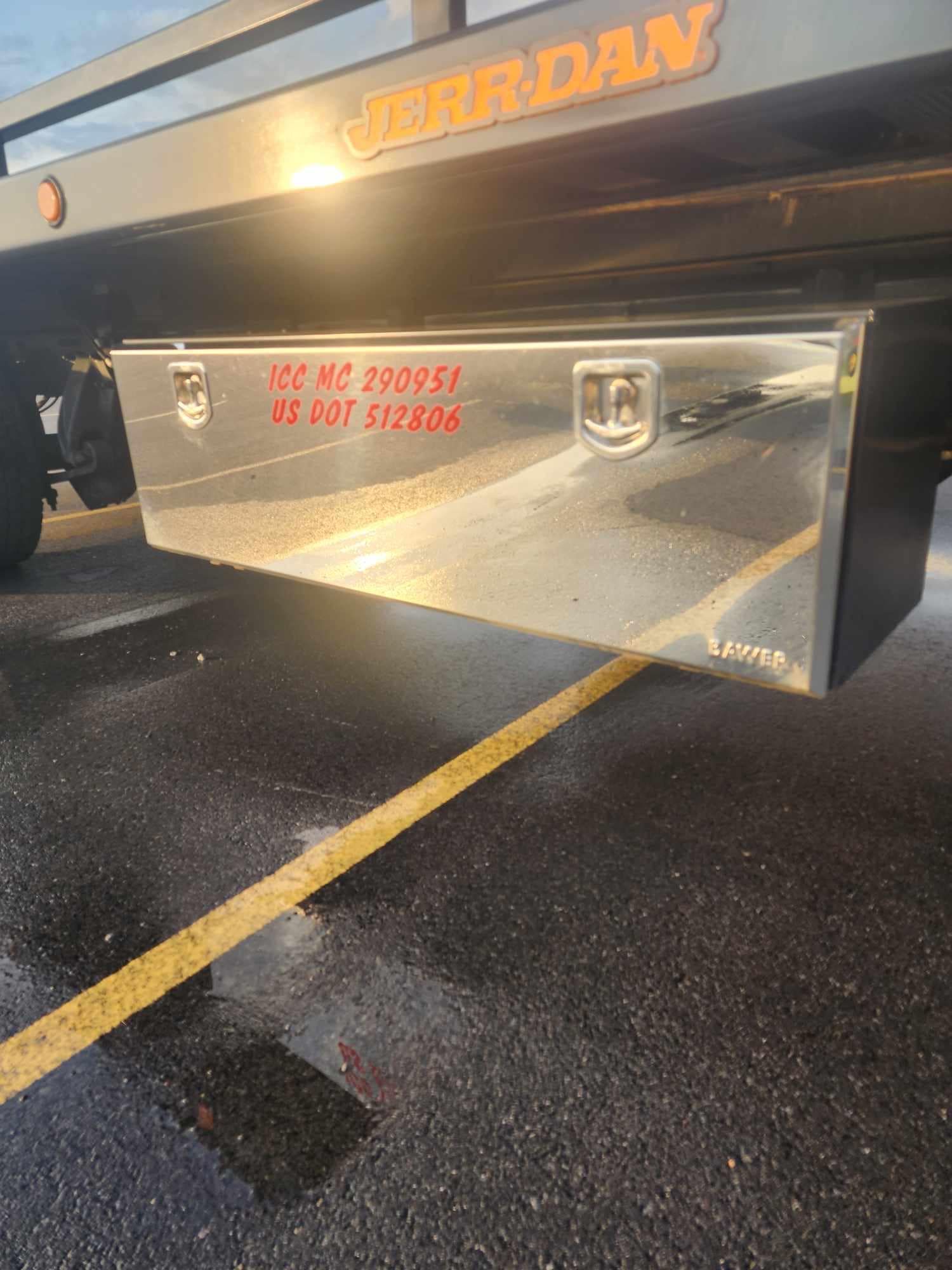 Shiny metal toolbox attached to a flatbed truck, with red lettering.