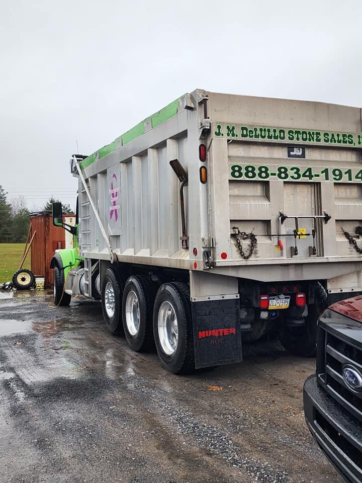 Dump truck with a green cab and silver bed, parked on a wet surface.