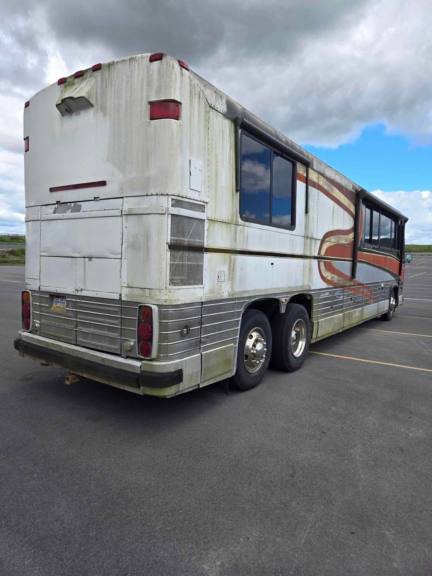 Dirty, white bus with side windows parked on asphalt under a cloudy sky.