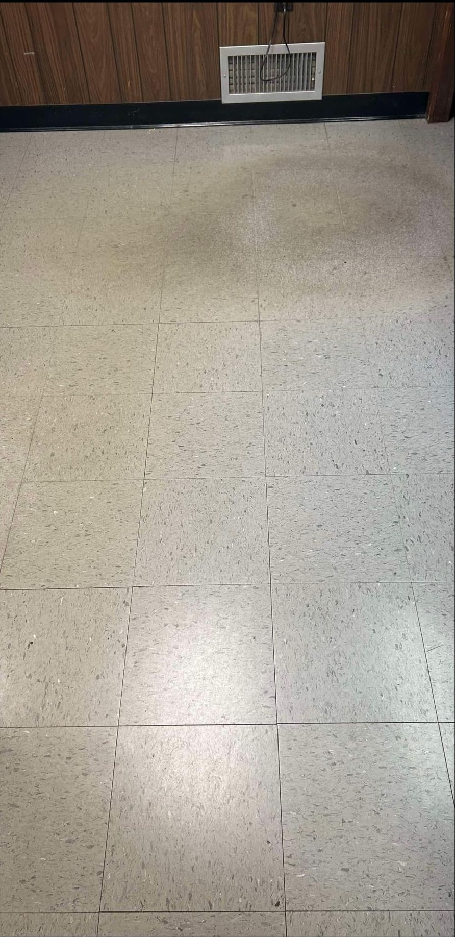A room with speckled tiles on the floor, wooden paneling on the walls and an air vent.