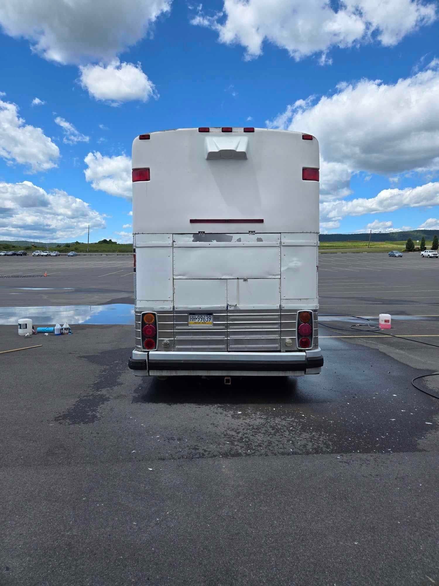 Back of a white bus with red accents on a parking lot under a blue sky.