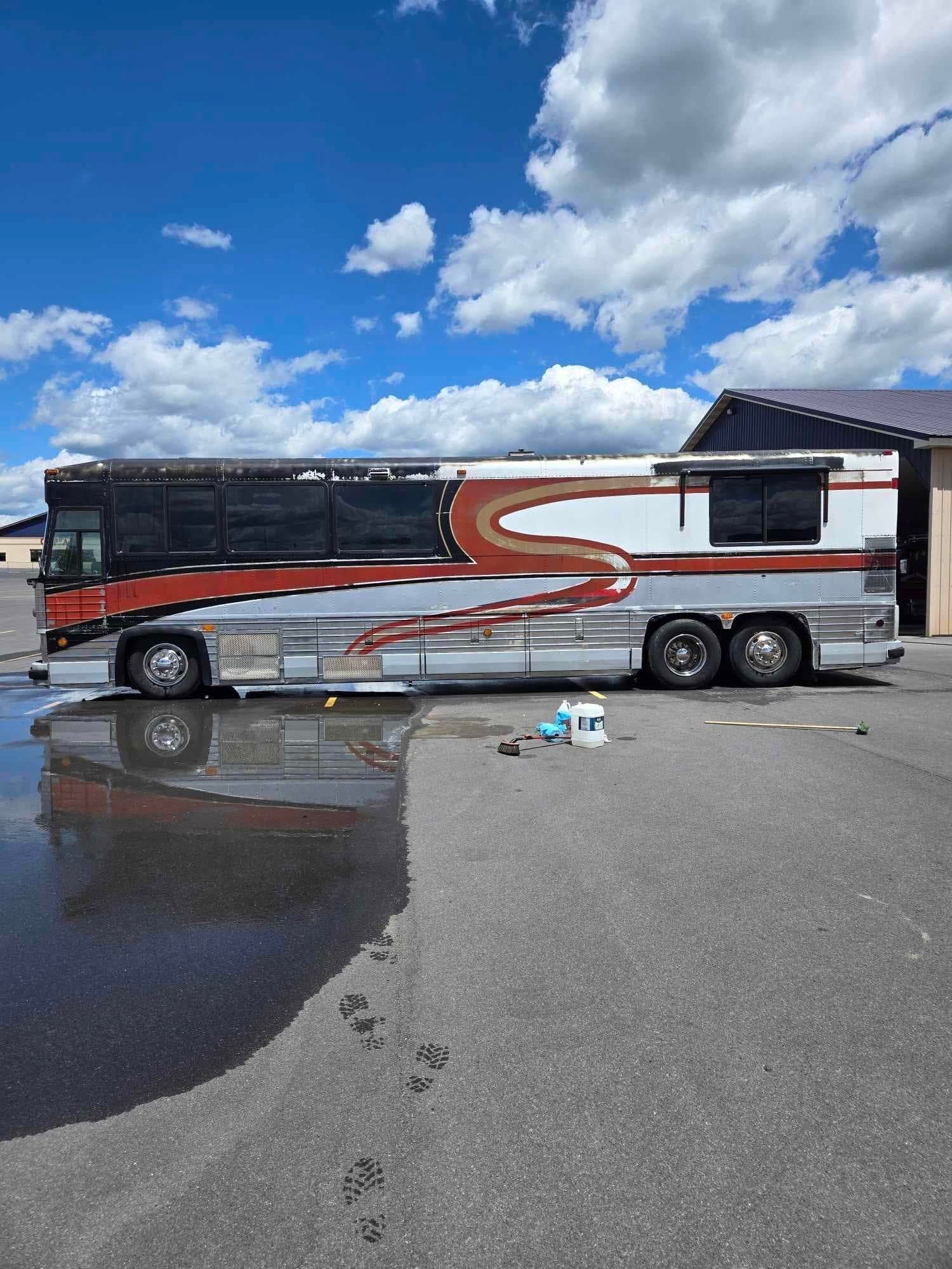 Side view of a large, colorful bus parked outside on a sunny day with wet pavement.