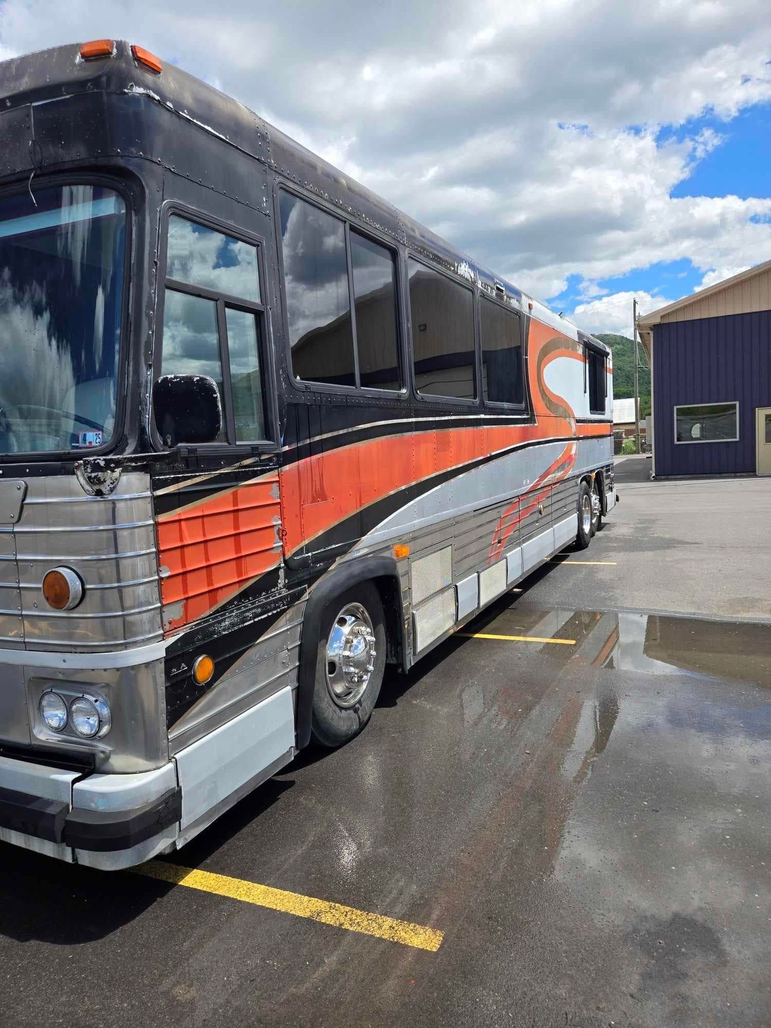 Side view of a large, black, orange, and silver motorcoach parked on wet pavement.