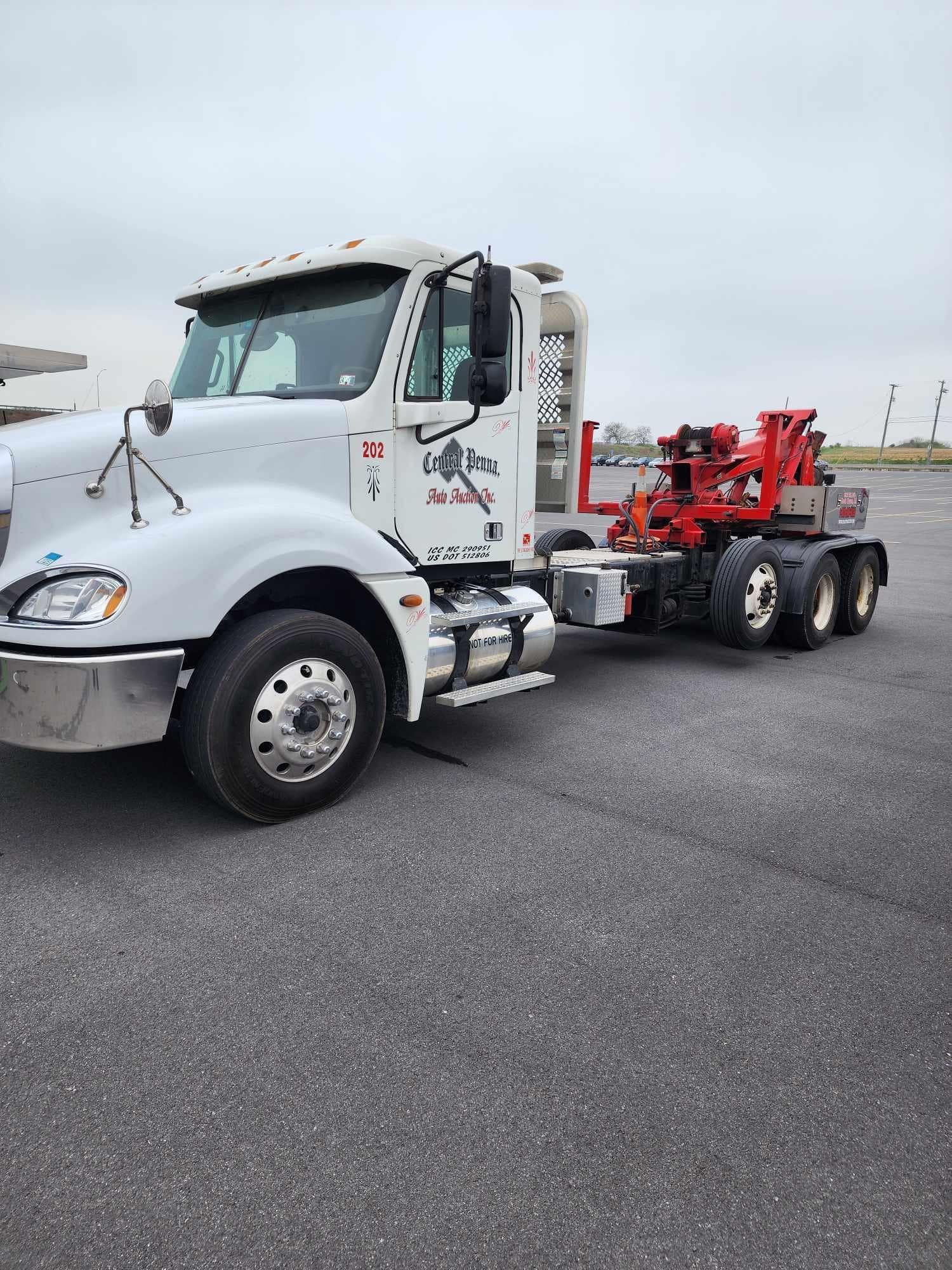 White tow truck with a red towing apparatus parked on asphalt.