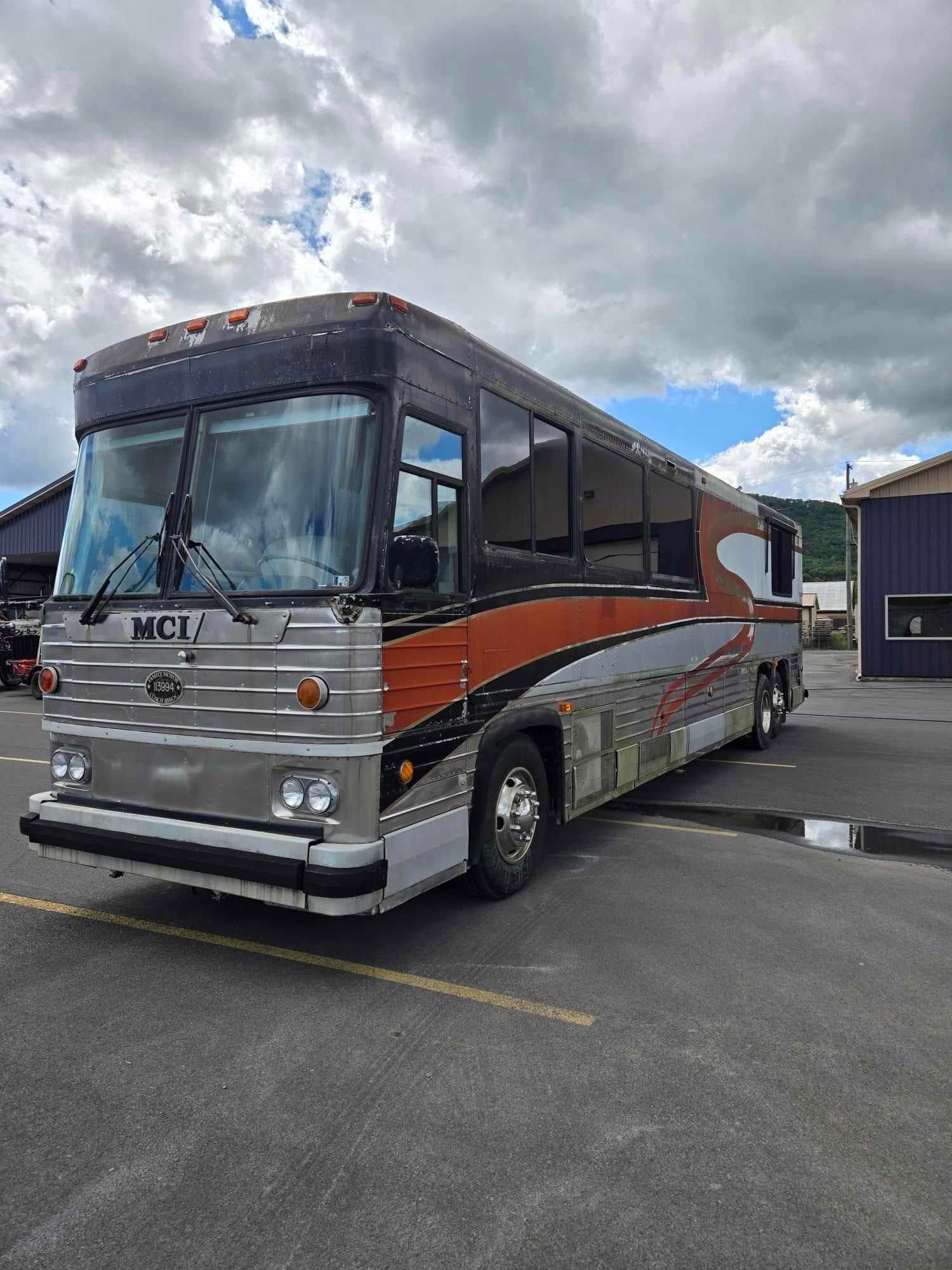 Motor Coach Industries (MCI) bus with orange and silver paint, parked in a lot.