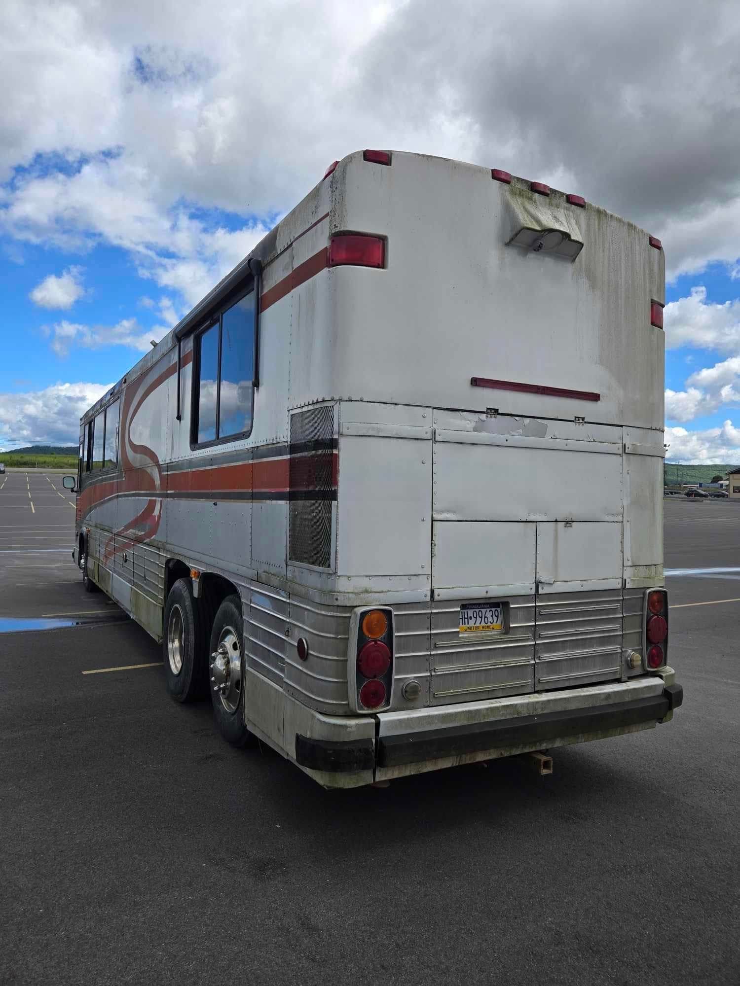 Rear view of a white and silver tour bus with red stripes parked on asphalt against a cloudy sky.