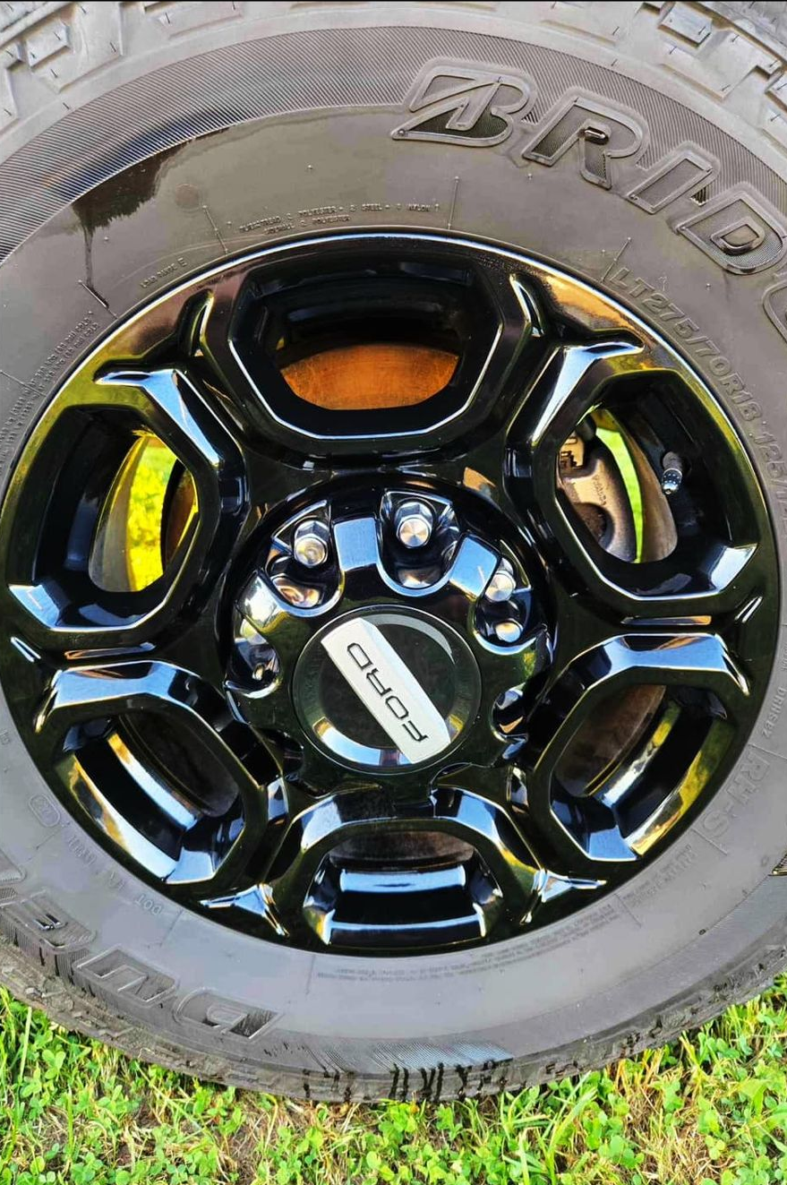 Black alloy wheel with a black center cap, mounted on a Bridgestone tire.