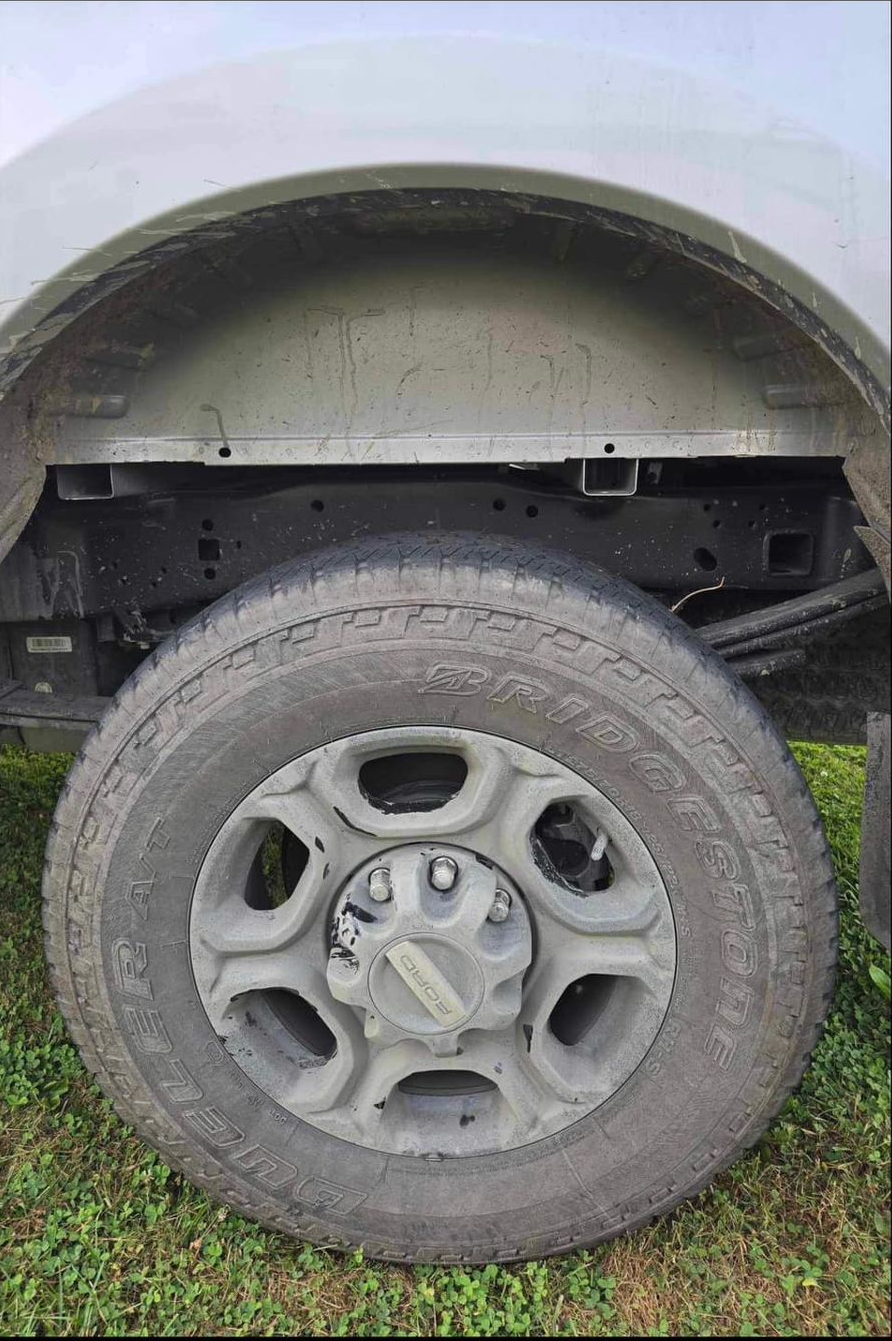 Truck tire and wheel well on grass. Gray, dirty wheel with many spokes.