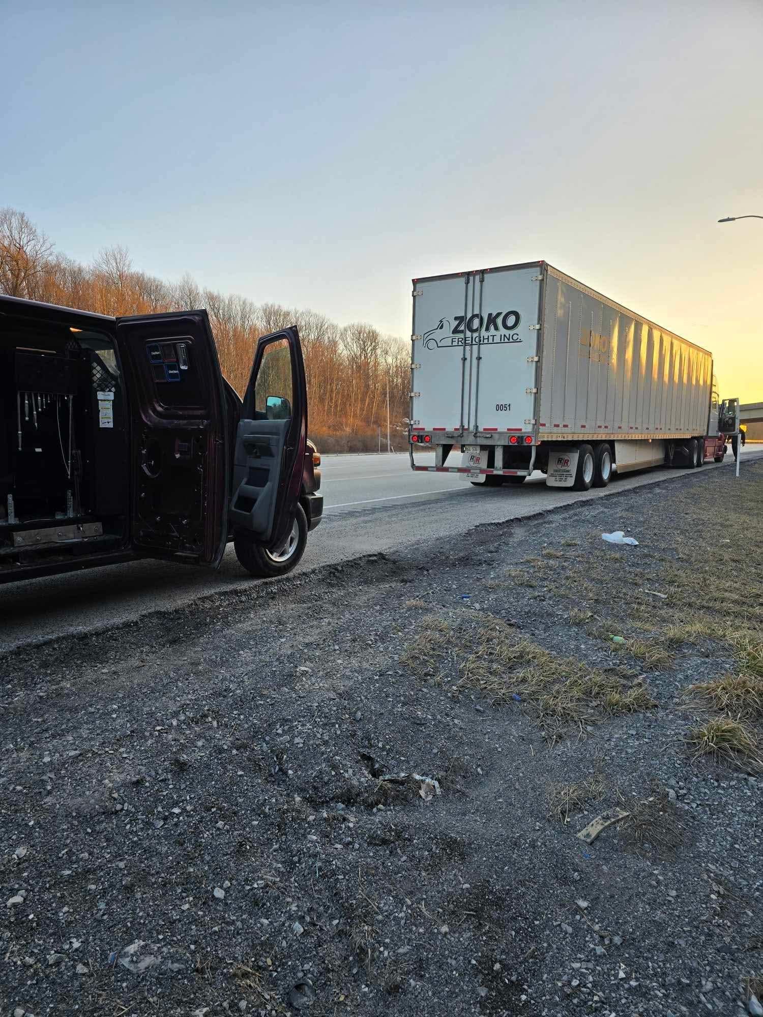 Dark pickup truck towing a white semi-trailer on a gravel road at sunset.