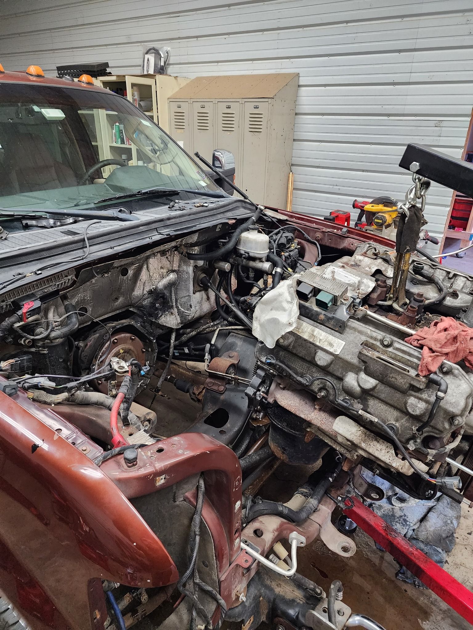 A truck's engine being removed in a garage. Red truck partially disassembled. Engine hoist in use.