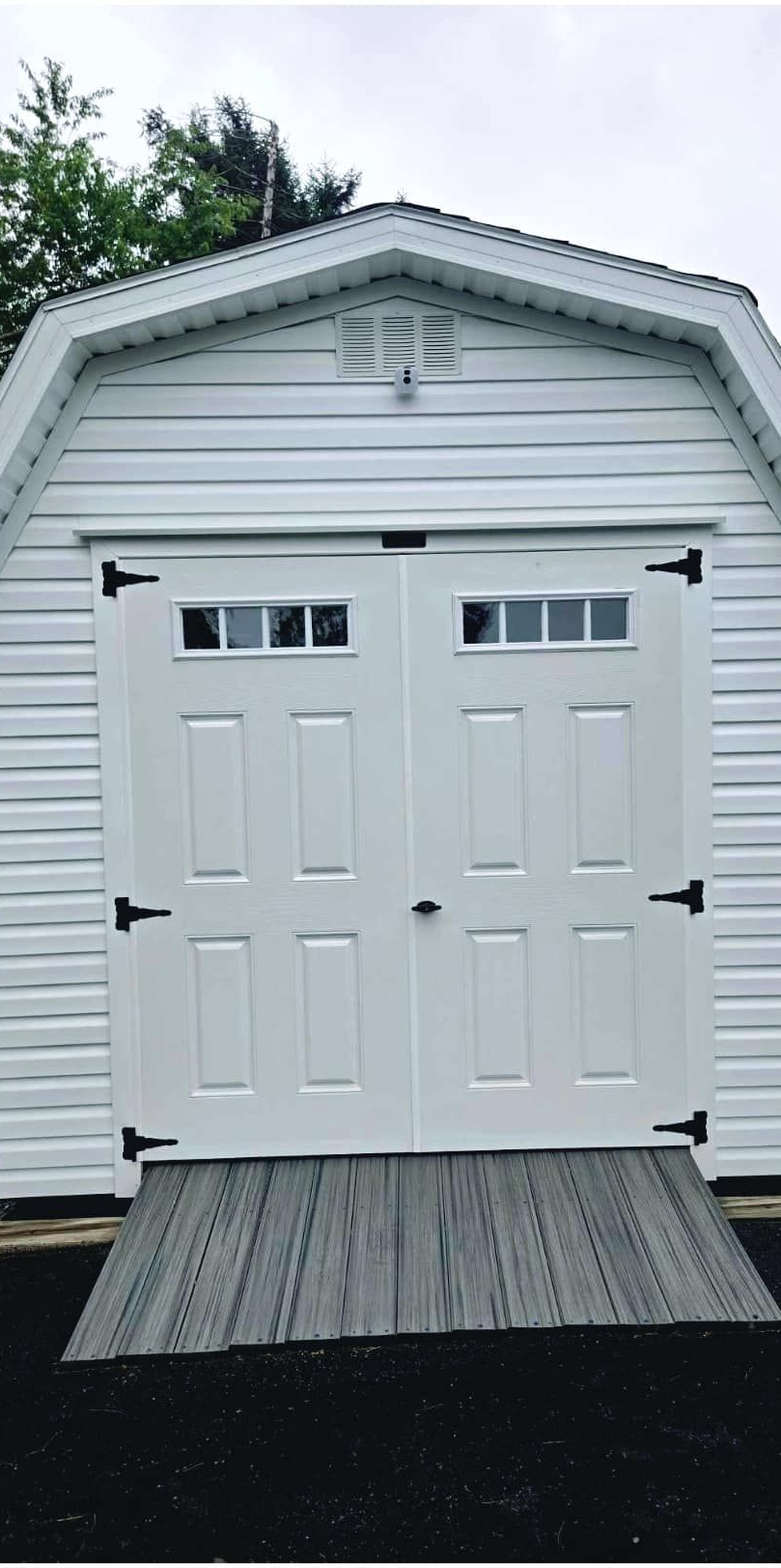White shed with double doors, black hardware, and a ramp. Cloudy sky.