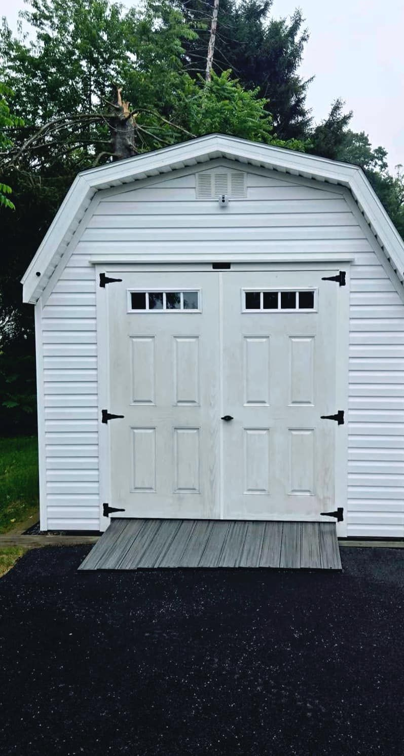 White shed with double doors, small ramp, and black hardware.