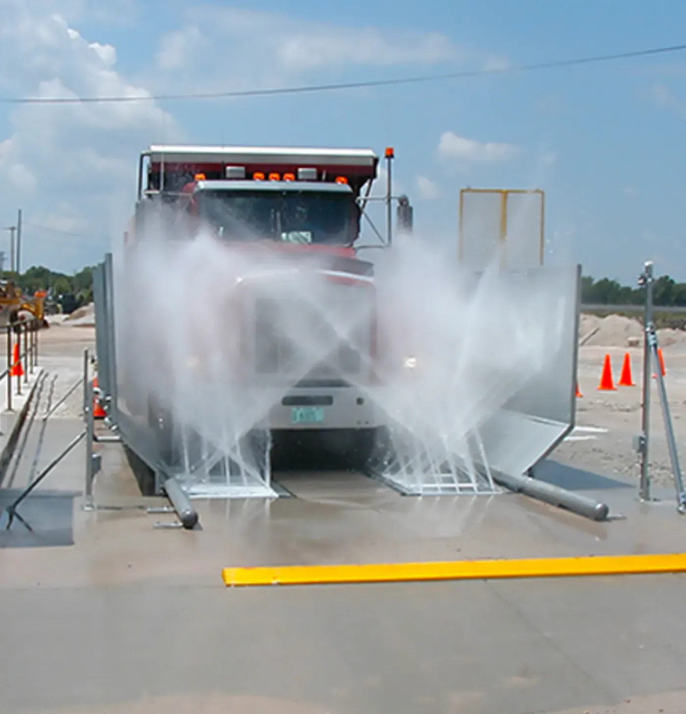 A truck being washed by water jets inside a metal enclosure, with orange cones in the background.